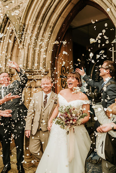 Exuberant bride and groom exiting a grand Yorkshire church, basking in a shower of confetti thrown by smiling guests, with the bride holding a lush bouquet, capturing the quintessential moment of celebration and union