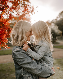 Mother and daughter gazing at each other with the sun behind them and a tree with red leaves to the side of them