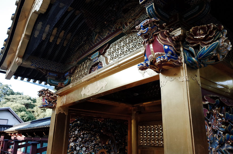 Ornate temple gate with gold detailing and colorful guardian sculptures in a serene outdoor setting, with trees and traditional architecture.