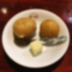 Two potatoes, a pat of butter, and a spoon on a white plate with "Bondy" logo. Set on a wooden table. Mood: simple and inviting.