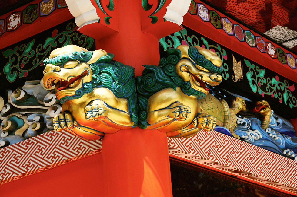 Golden lion carvings with green manes on a vibrant red and black temple structure, featuring intricate patterns and colorful details.
