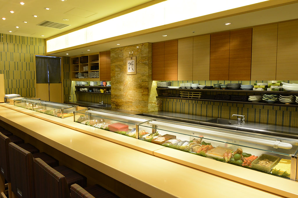Sushi bar with empty seats, a glass display of fresh seafood, wooden cabinets, and patterned walls. Warm lighting creates a cozy ambiance.