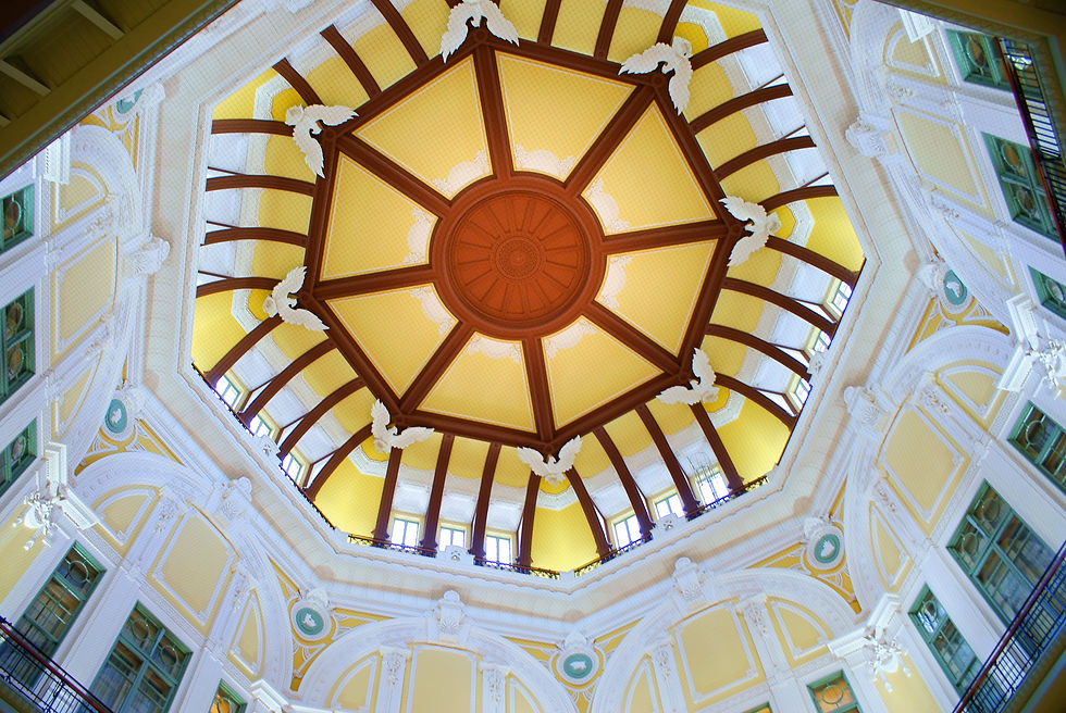 Ornate dome ceiling with yellow and brown geometric patterns, white arches, and decorative motifs, viewed from below in a bright setting.