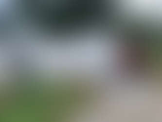 White shipping container on gravel, next to a white building. Red text on container. Greenery and trees in background. Overcast sky.