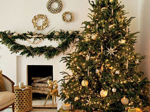 Elegant holiday table setting with white dishes, gold cutlery, and greenery. Candlelit with bokeh lights and decorated Christmas tree.