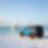 a 4 door blue Jeep on a white sandy beach in the florida keys with a sailboat with green c