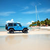 blue 4 Door Jeep on a caribbean island beach with a sailboat moored nearby.jpg
