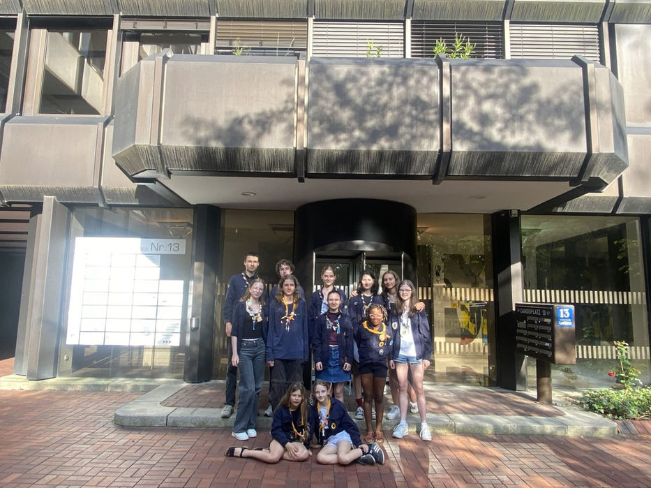 Pfadfindergruppe vor einem Gebäude: Alle tragen Halstücher und posieren fröhlich für ein Gruppenfoto.