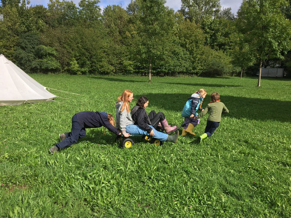 Geländespiel auf der Wiese: Kinder ziehen einander auf einem selbstgebauten Gefährt – kreative Outdoor-Aktivität.
