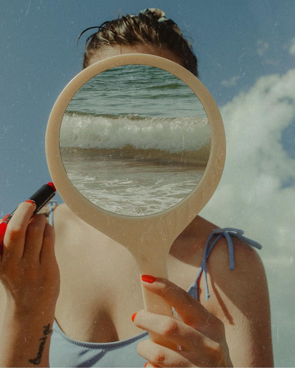 Donna con specchio che riflette il mare, simbolo di identità, introspezione e connessione tra immagine esteriore e mondo interiore.