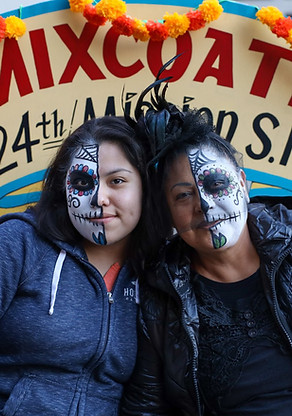 Two women with painted faces celebrating Día de Muertos in front of the Mixcoatl store.