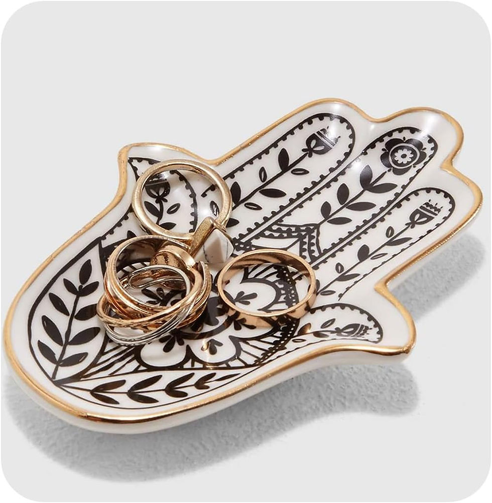 Hand-shaped white trinket dish with black floral pattern and gold trim holding several rings on a white background