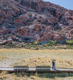 Couple on a desert boardwalk with rocky mountains behind.