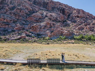 Couple on a desert boardwalk with rocky mountains behind.