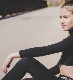 Girl in black sportswear sitting outdoors leaning on a wall