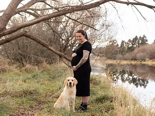 Pregnant mum standing by river with her golden retriever dog