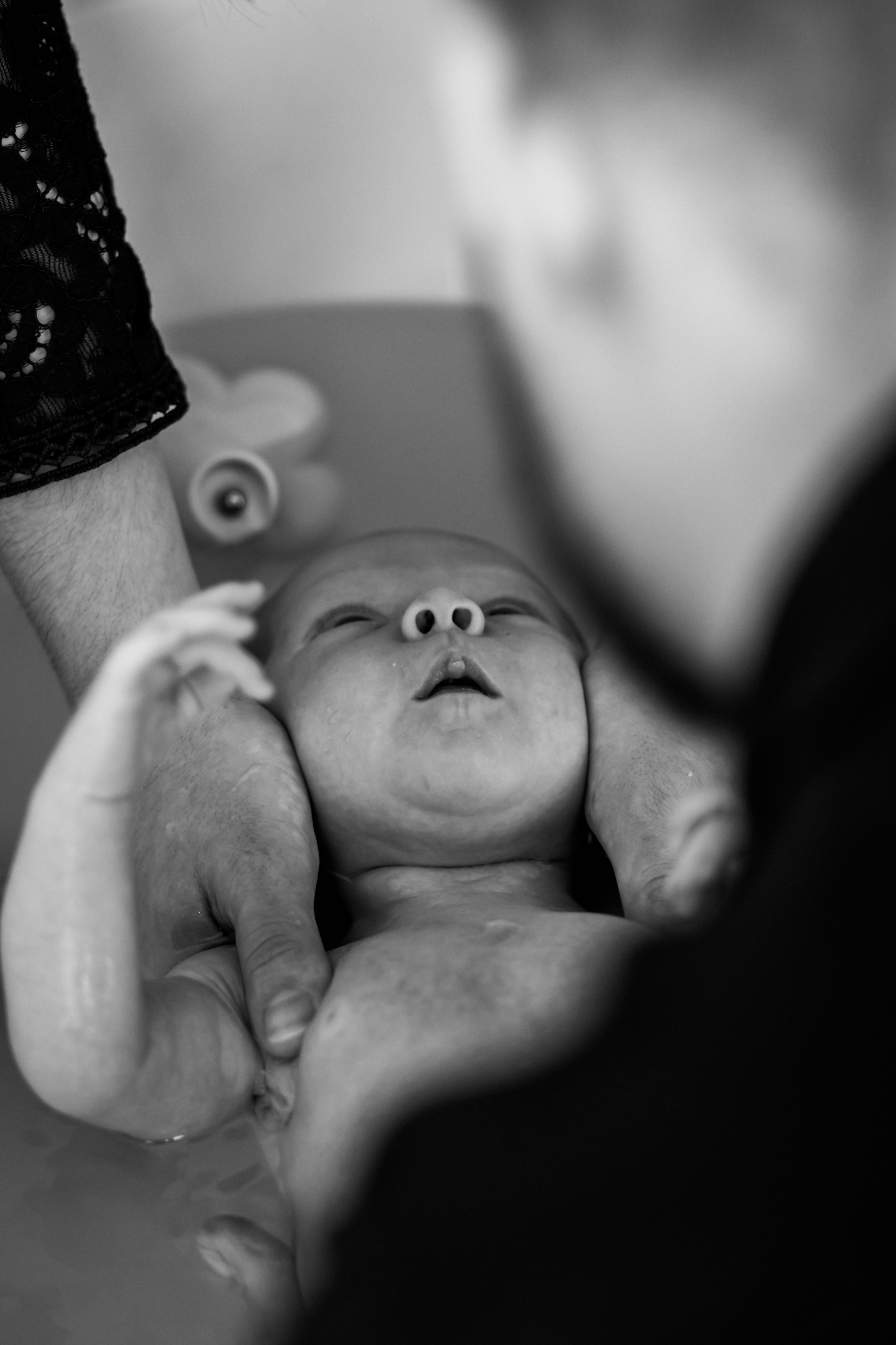 bébé apaisé dans son bain entouré des mains de ses deux parents. 
