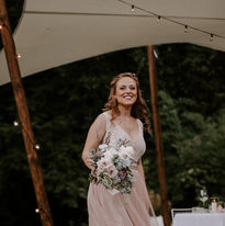 Braut in einem rosa Brautkleid lächelt in die Kamera mit einem Brautstrauß in der Hand 