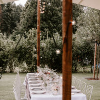 Ein Hochzeitstisch im Garten unter Lichterketten in einem Zelt 