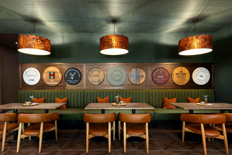 Cozy cafe with green banquette seating and brown chairs. Round decor on walls under warm pendant lights. Relaxed, inviting atmosphere. Cask Whisky Bar Grand Cayman