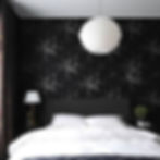 Bedroom with black floral wallpaper, white quilted bed, hanging lamp, and a nightstand with a lamp and plant, creating a cozy ambience.