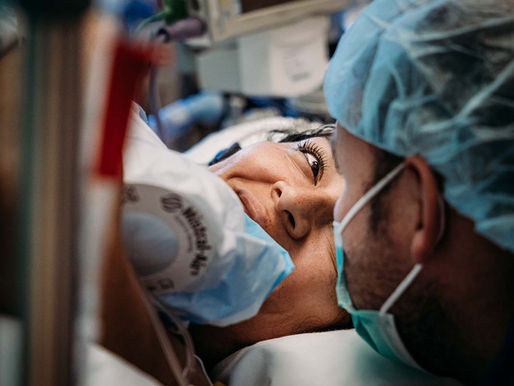 Een moeder ligt op de operatietafel na een keizersnede en kijkt haar partner liefdevol aan – een intiem en emotioneel moment direct na de geboorte van hun baby.