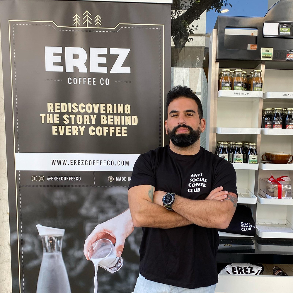 Oleh Matan Bouganim standing in front of a sign of his coffee shop, Erez
