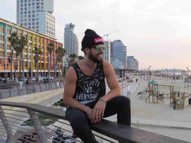 Oleh Johnny Denver Levine sitting on a fence railing on the beach in Tel Aviv