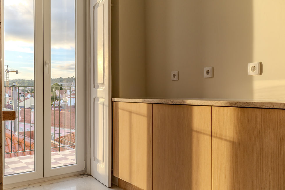 Kitchen detail in a four-bedroom apartment in Lapa, Lisbon, with floor-to-ceiling balcony doors, custom wooden cabinetry, stone countertop, and warm afternoon light entering the space.