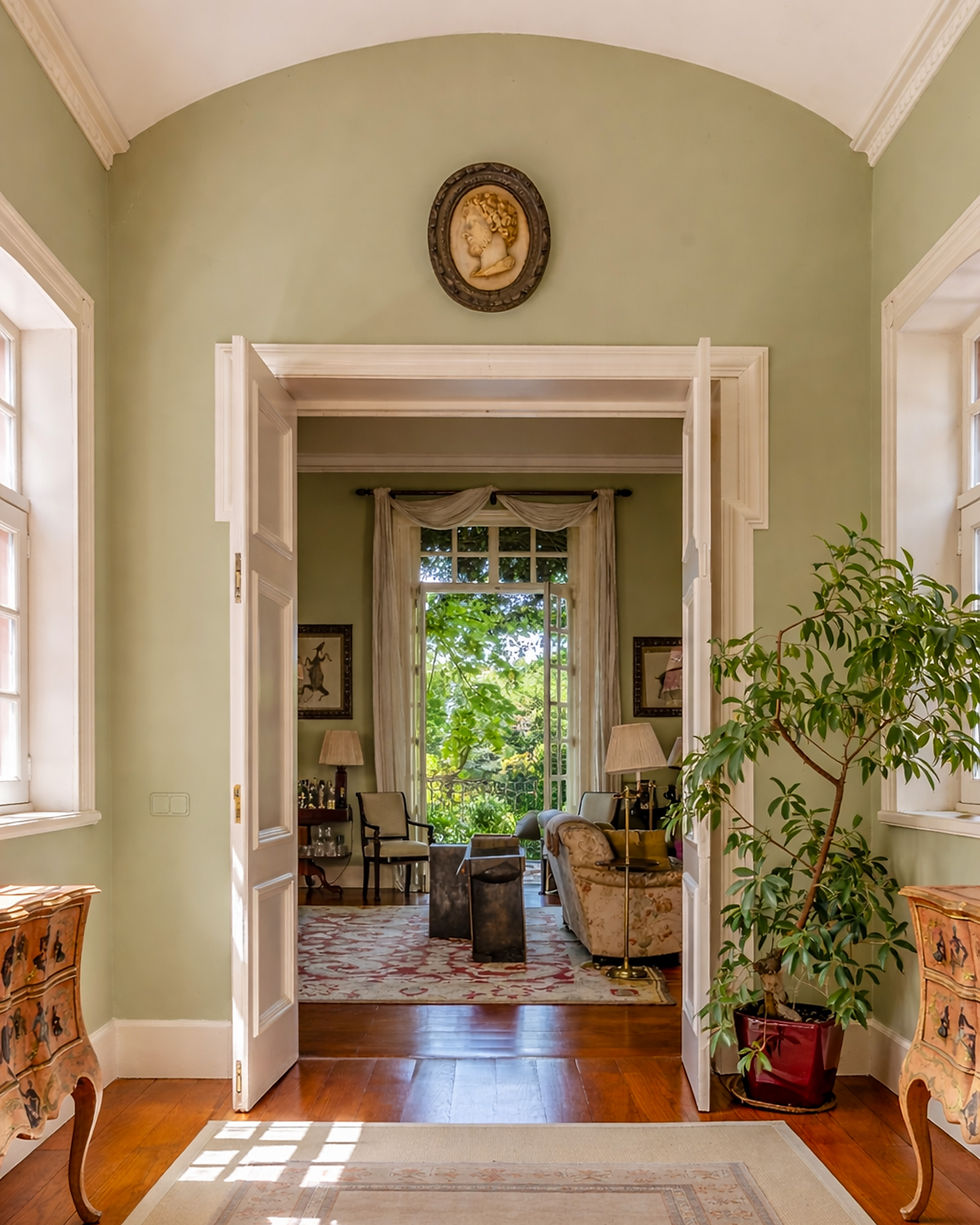 Elegant interior hallway with arched ceiling, soft green walls and original wooden floors, opening onto a refined living room with garden views at a country residence in Cantanhede, Coimbra, Portugal.