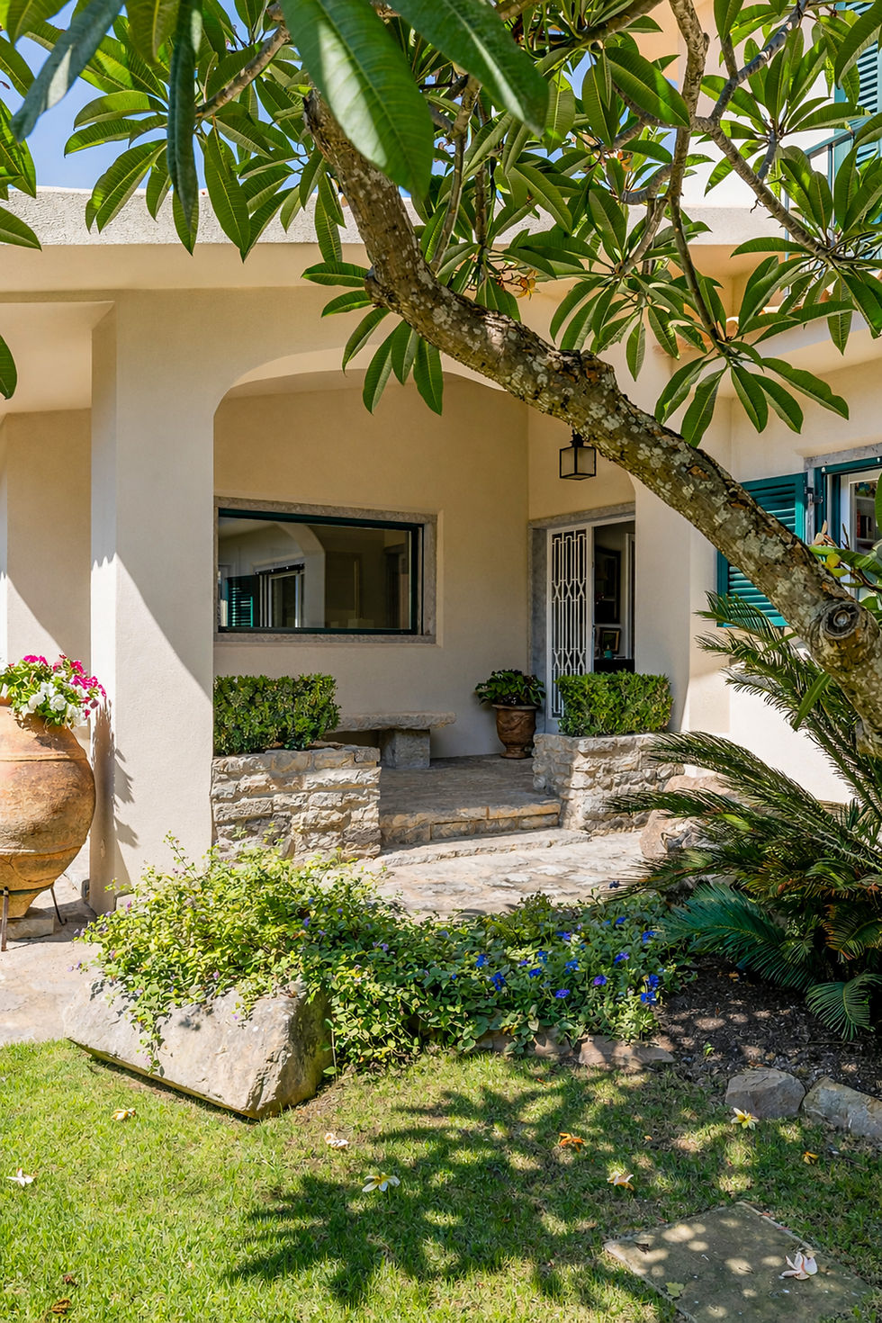 Charming covered entrance framed by lush Mediterranean landscaping, stone details, and mature trees, creating a serene outdoor atmosphere in this Cascais townhouse.