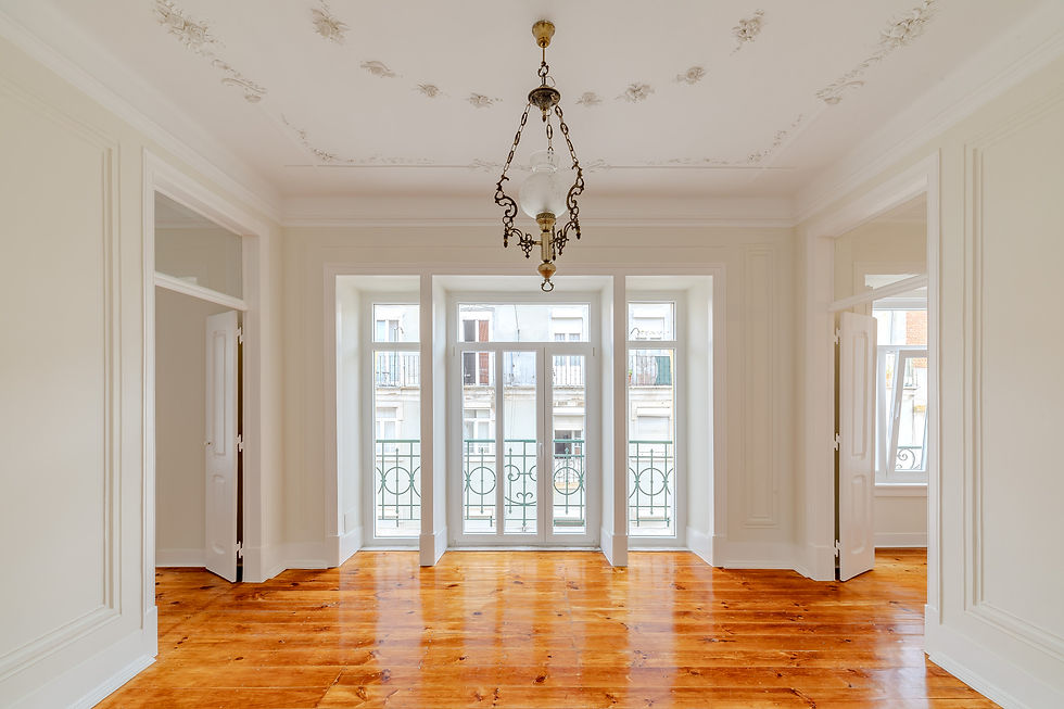 Elegant living room in a four-bedroom apartment in Lapa, Lisbon, with original wooden floors, high ceilings with decorative plasterwork, classic chandelier, and large French windows opening onto wrought-iron balconies.