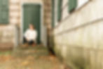 Young teen girl kneeling in front of green double doors where the camera is close to a cedar planked wall.