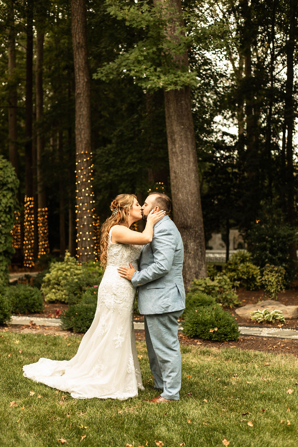 Sussex county's willowbrook wedding venue has a forest of trees leading up to their brick wall ceremony backdrop. Couple is standing kissing with the trees covered in tiny lights.