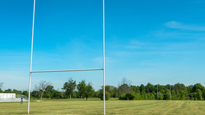 Rugby goalposts rising above a grass rugby pitch under a clear blue sky