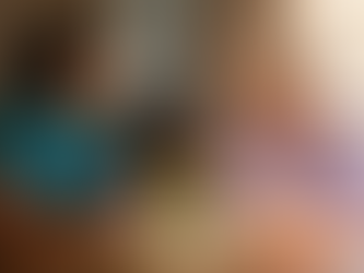 A Black female caregiver in teal scrubs with natural hair pulled back listens attentively and takes notes at a sunlit kitchen table across from an elderly white woman with short silver hair and a lavender cardigan as they discuss her personalized home care plan together.
