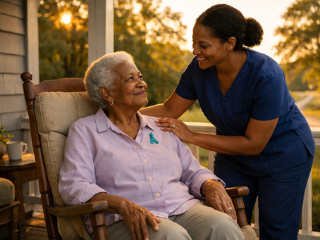 Smiling caregiver in blue scrubs comforts an elderly woman in a rocking chair on a sunlit porch at sunset.