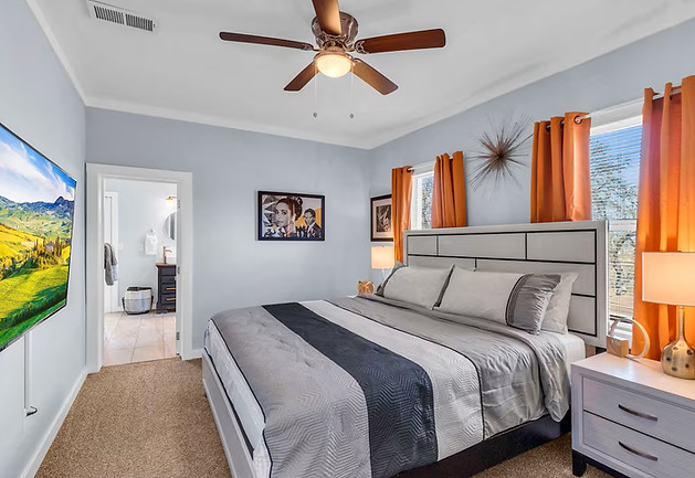 Bright bedroom with king sized bed, TV, two windows, and end tables. The color scheme is white, black, and orange.