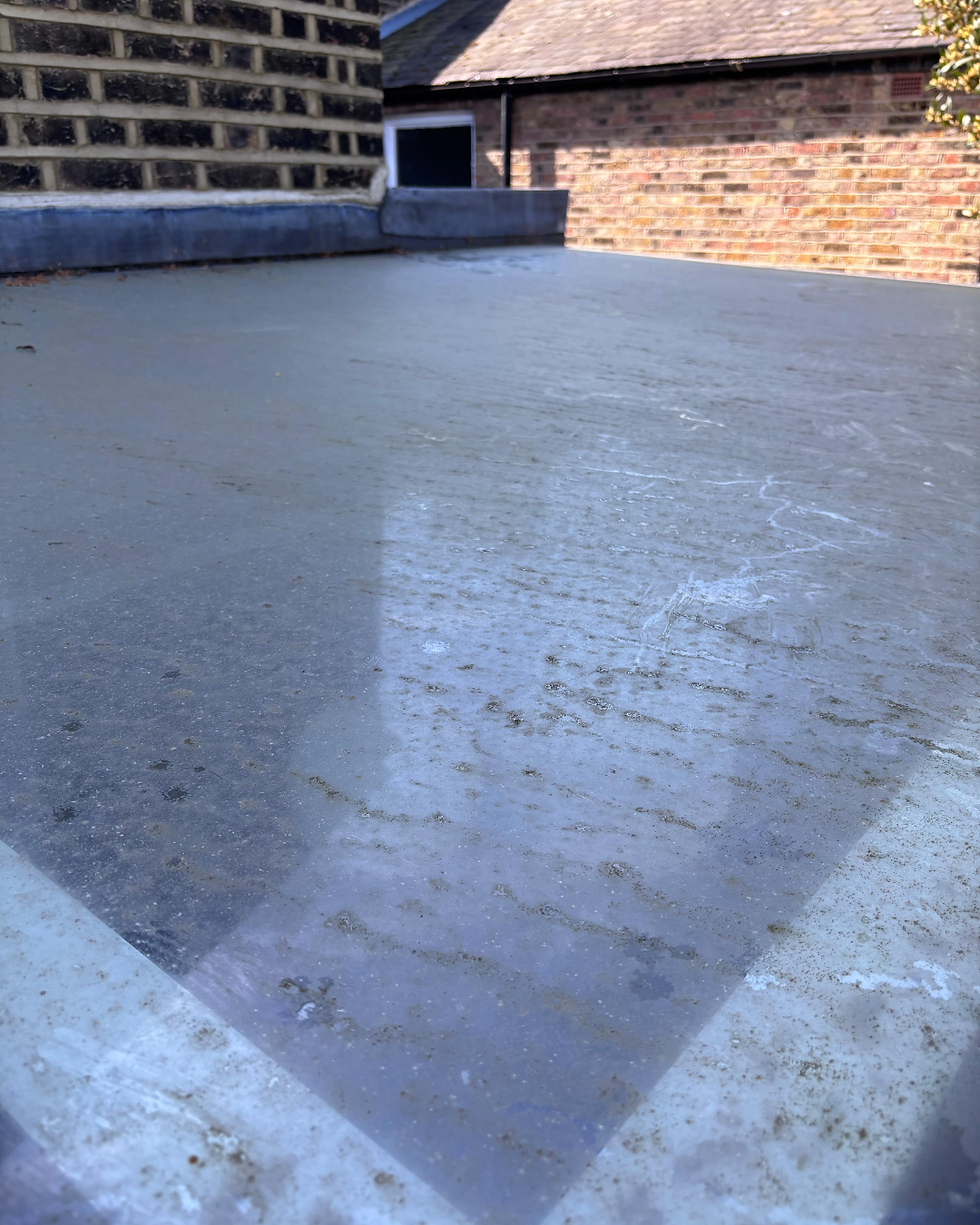 A glass roof covered in thick layer of dirt build-up beside brick buildings.