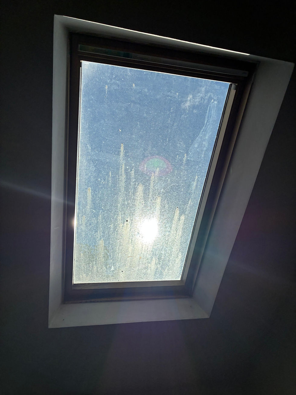 Dirty skylight window in a dark room, sunlight glaring through the glass with lens flare.