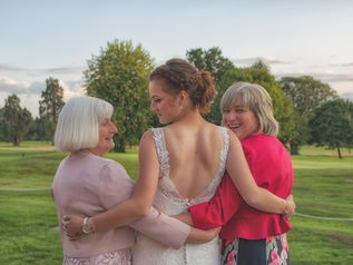 Bride stands with her arms around mum and grandmother in front of the golf course at Gosfield Lake Golf Club