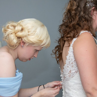 Bridesmaid in pale blue uses a crichet hook to do up the buttons on the back of the brides dress