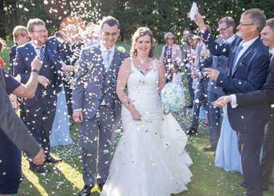 Bride and groom in the sunshie are showered with confetti