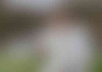 Groom stands behind his bride and kisses her cheek by the lake at Crondon park