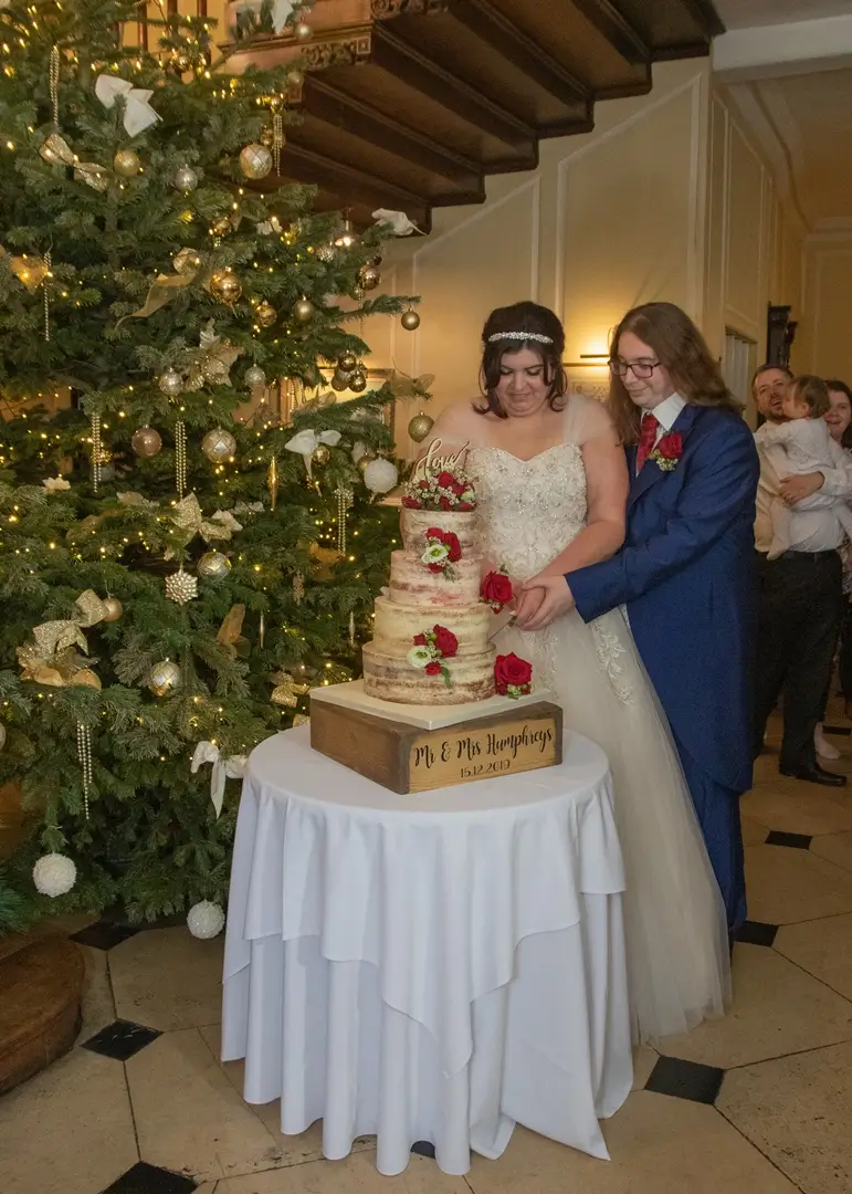 Bride and groom cut their wedding cake by a Christmas tree at Gosfield Hall