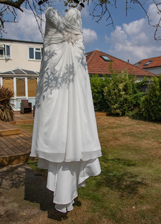 Wedding dress hanging from a tree in the brides parents garden with sunshine, blue sky and white puffy clouds