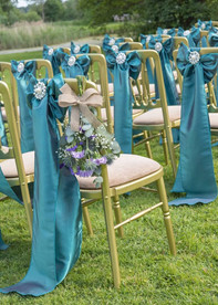 Outdoor wedding ceremony chairs decorated with  green sashes, thistles and flowers at Prested Hall