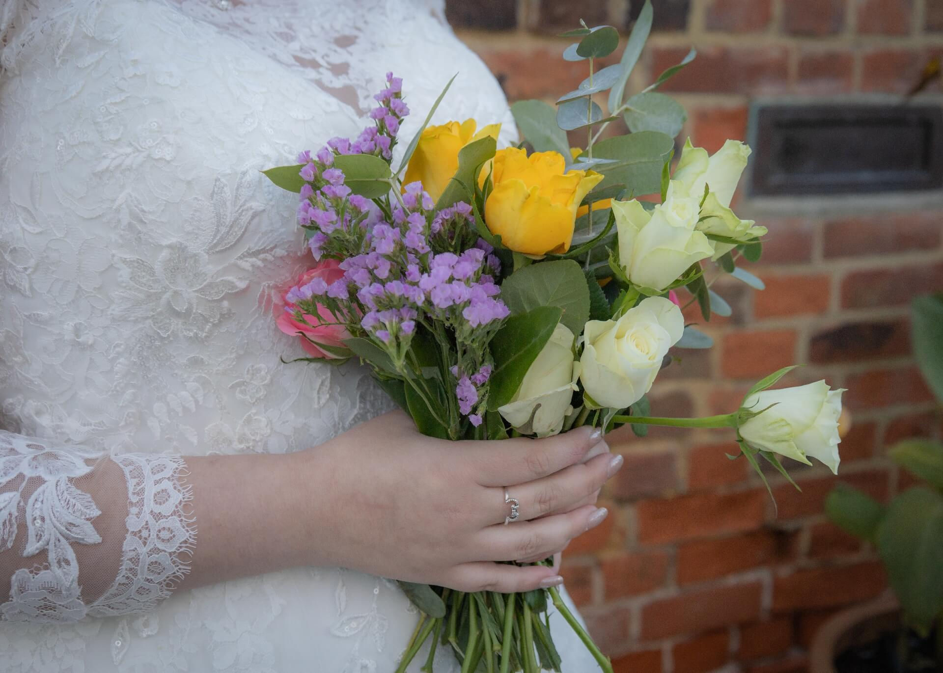 Bride holds her hand tied wedding bouquet of mixed flowers