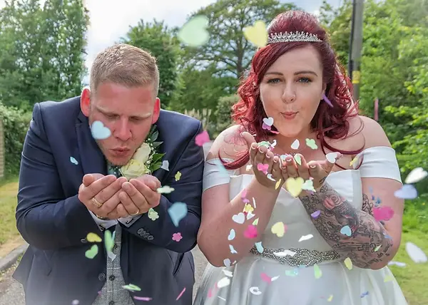Bride and groom blowing confetti towards the camera