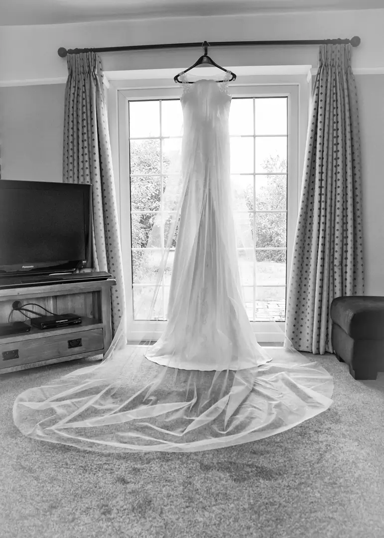 Wedding dress and veil hanging in the brides house during morning preparations